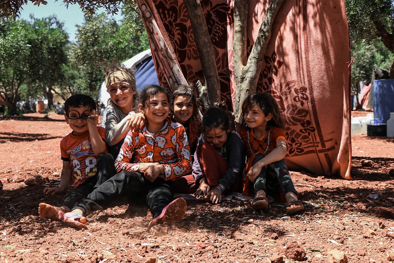 Group of happy children playing and smiling outdoors in a refugee camp in Idlib, Syria.